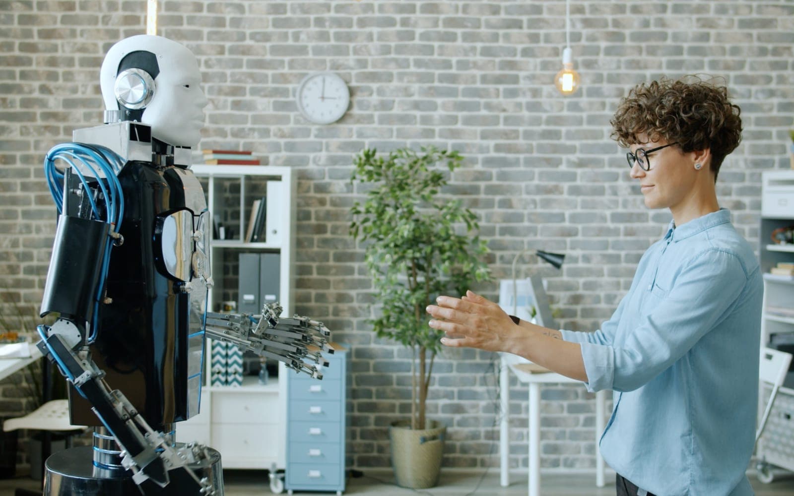 A person reaching out to a humanoid robot in a bright office